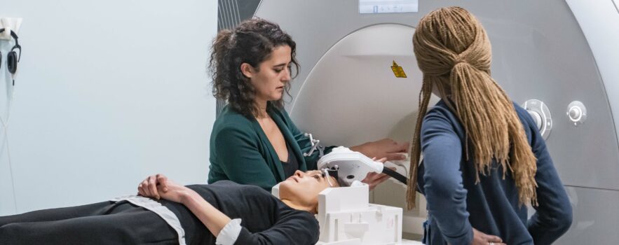 Person lying on a MRI bed getting ready to be scanned for a TMS (Transcranial magnetic stimulation) study. One scientist and a radiographer are setting up the experiment.